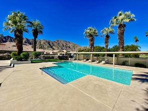 Ein Swimmingpool mit Liegestühlen, Palmen und einem Berg im Hintergrund.