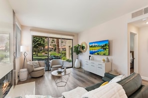 Ein geräumiges Wohnzimmer mit einem großen Schiebeglastür, die auf einen Balkon führt, einem bequemen Sofa, einem Couchtisch und einem an der Wand montierten Flachbildfernseher.