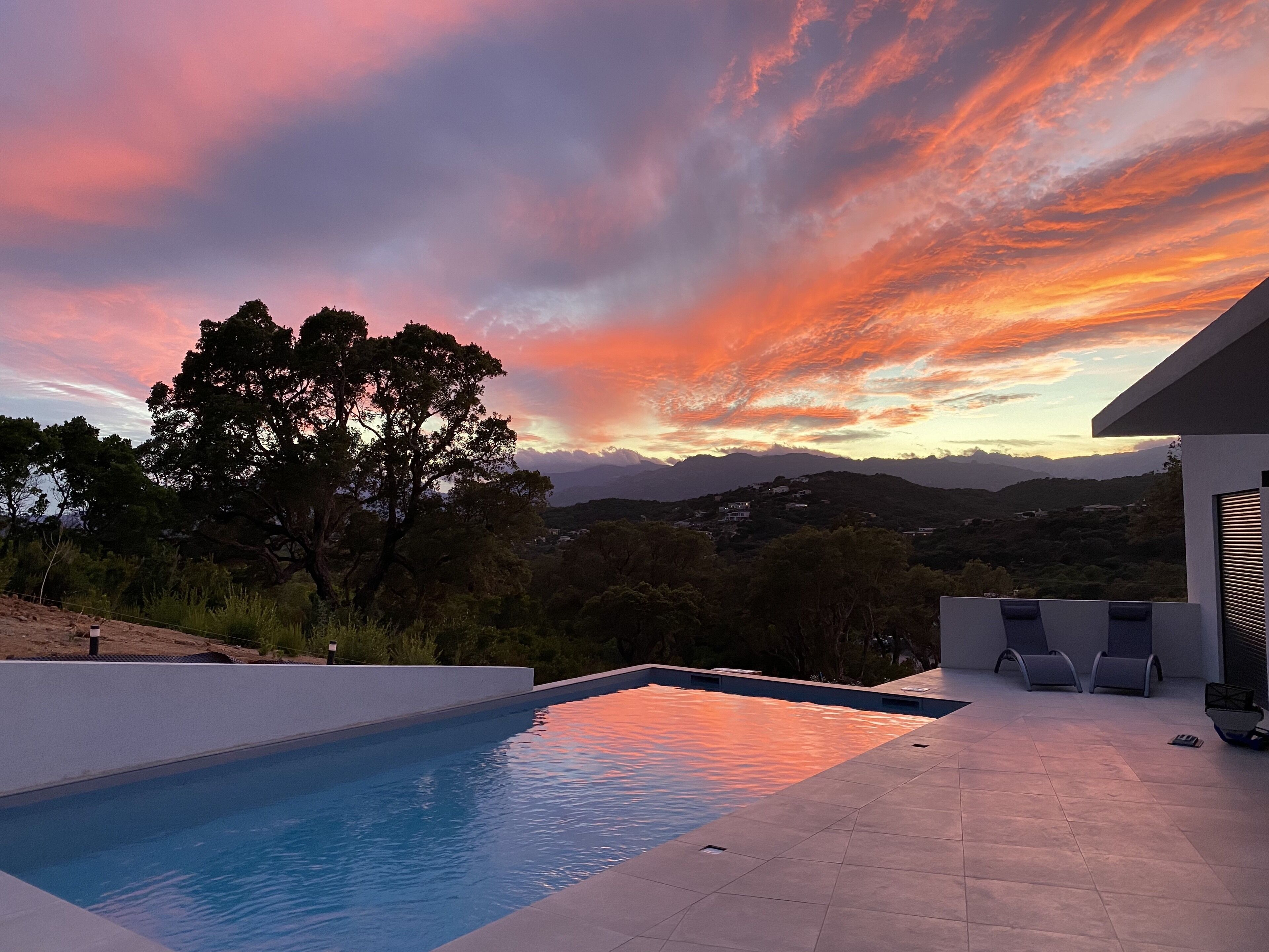 A swimming pool with a view of a sunset and mountains in the background.