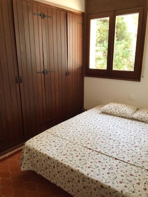 A bedroom with a bed, floral bedspread, and a wardrobe with a window.