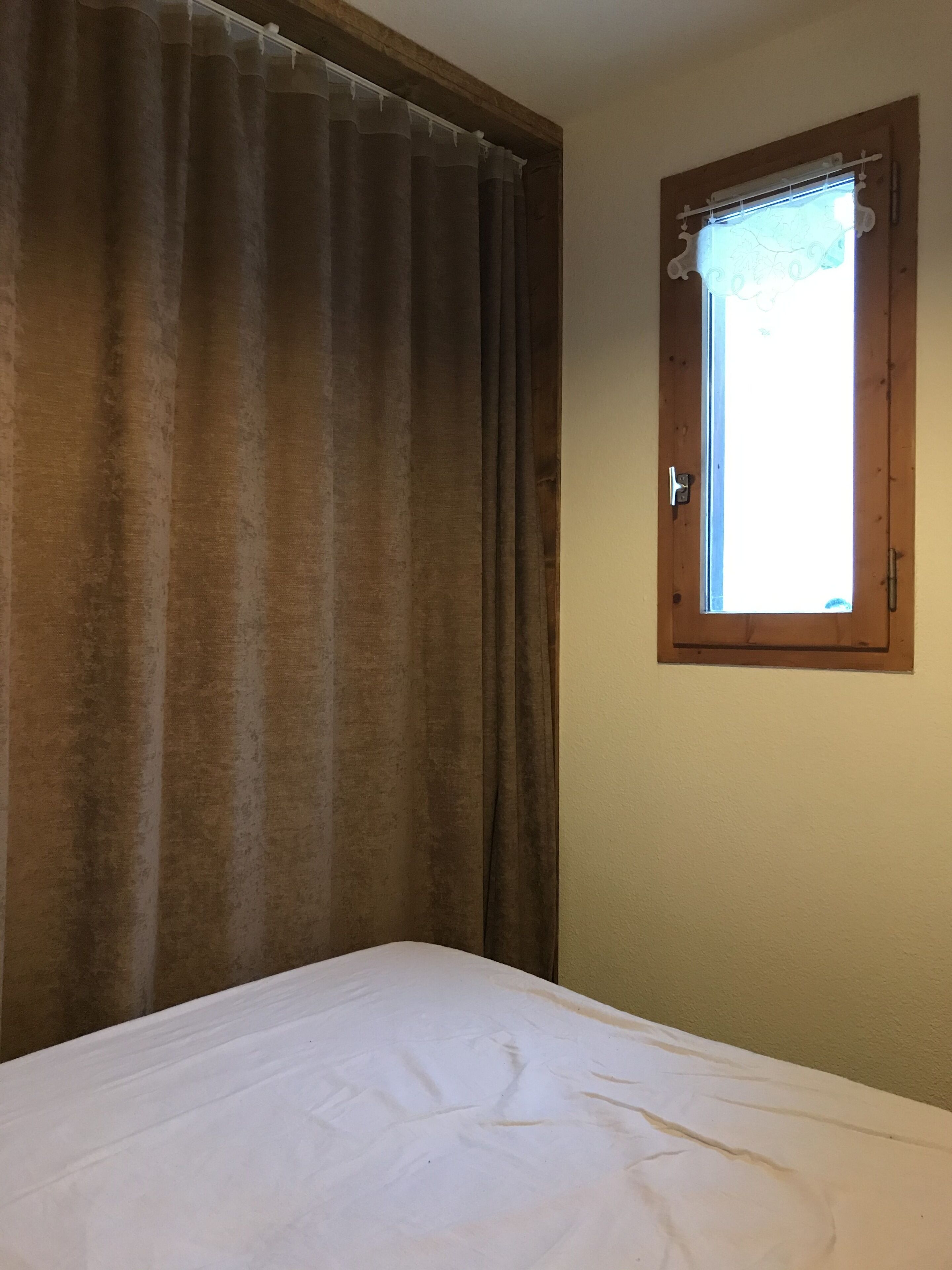 A room with a bed, a window with a curtain, and a door.