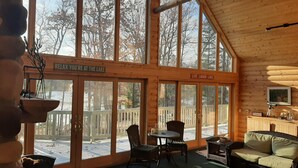 A cozy cabin with large windows, a wooden deck, a dining area, and a living room furnished with a sofa and chairs. - Round Lake Cabin Retreat (Hayward)