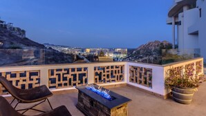 A rooftop terrace with a fire pit, seating, and a view of a cityscape at dusk. - PERFECT for large families/groups! 7 luxurious Guest Suites. Amazing Views! (cabo san lucas)