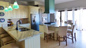 A kitchen with a central island, a stove, and a sink. There are chairs around the island and a dining table with chairs. - PERFECT for large families/groups! 7 luxurious Guest Suites. Amazing Views! (cabo san lucas)