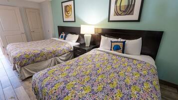 A hotel room with two beds, each with floral-patterned bedding, a nightstand with a lamp, and abstract artwork on the walls.
