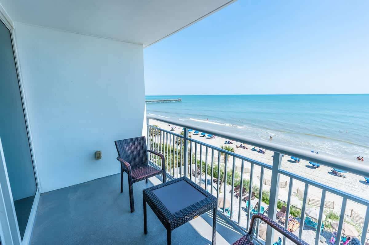 Un balcon meublé avec des meubles en osier, donnant sur une plage et un quai.