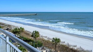 A beach with a wooden pier extending into the ocean, a sandy shoreline, and a few palm trees. - Remodeled 5th Floor Condo All Tile Near Boardwalk! (Myrtle Beach)