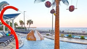 A swimming pool with a dolphin sculpture, palm trees, and a view of the ocean. - Remodeled 5th Floor Condo All Tile Near Boardwalk! (Myrtle Beach)