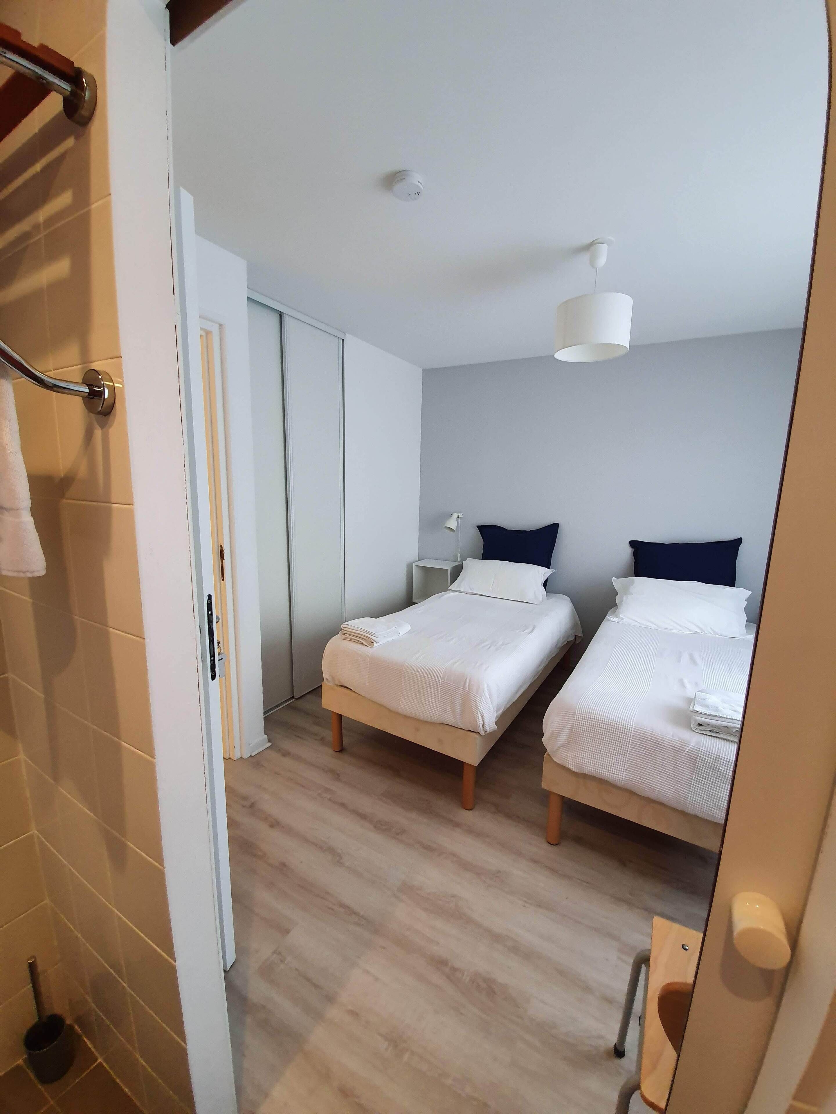 Une chambre d’hôtel avec deux lits simples, un plancher en bois, un plafond blanc et une porte donnant sur une salle de bain.