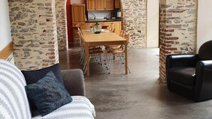 Een woonkamer met een bank, een eethoek met een houten tafel en stoelen, en een keuken die door een boog zichtbaar is.