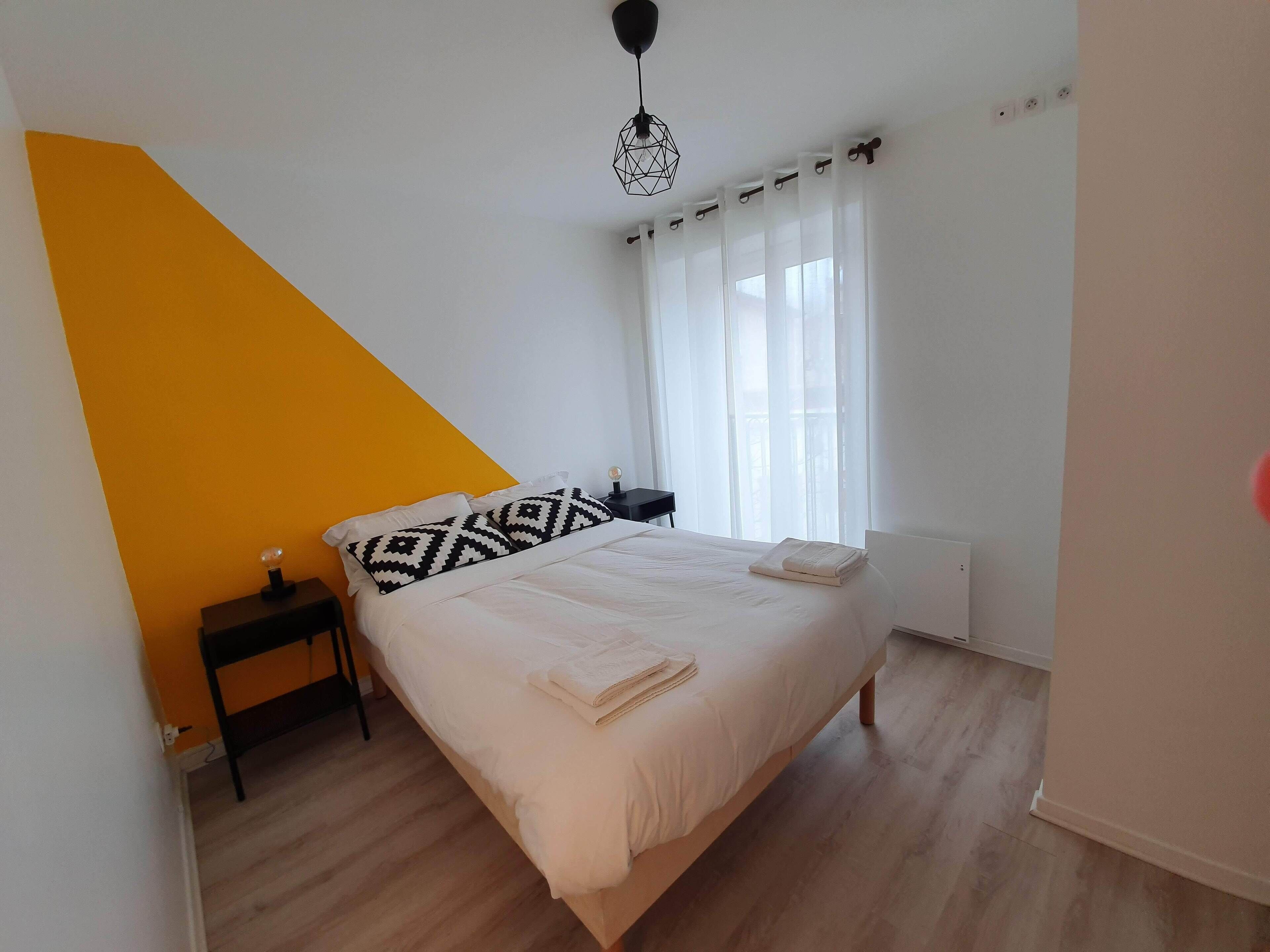 Une chambre à coucher avec un lit, une table de chevet, une lampe et une fenêtre avec des rideaux.