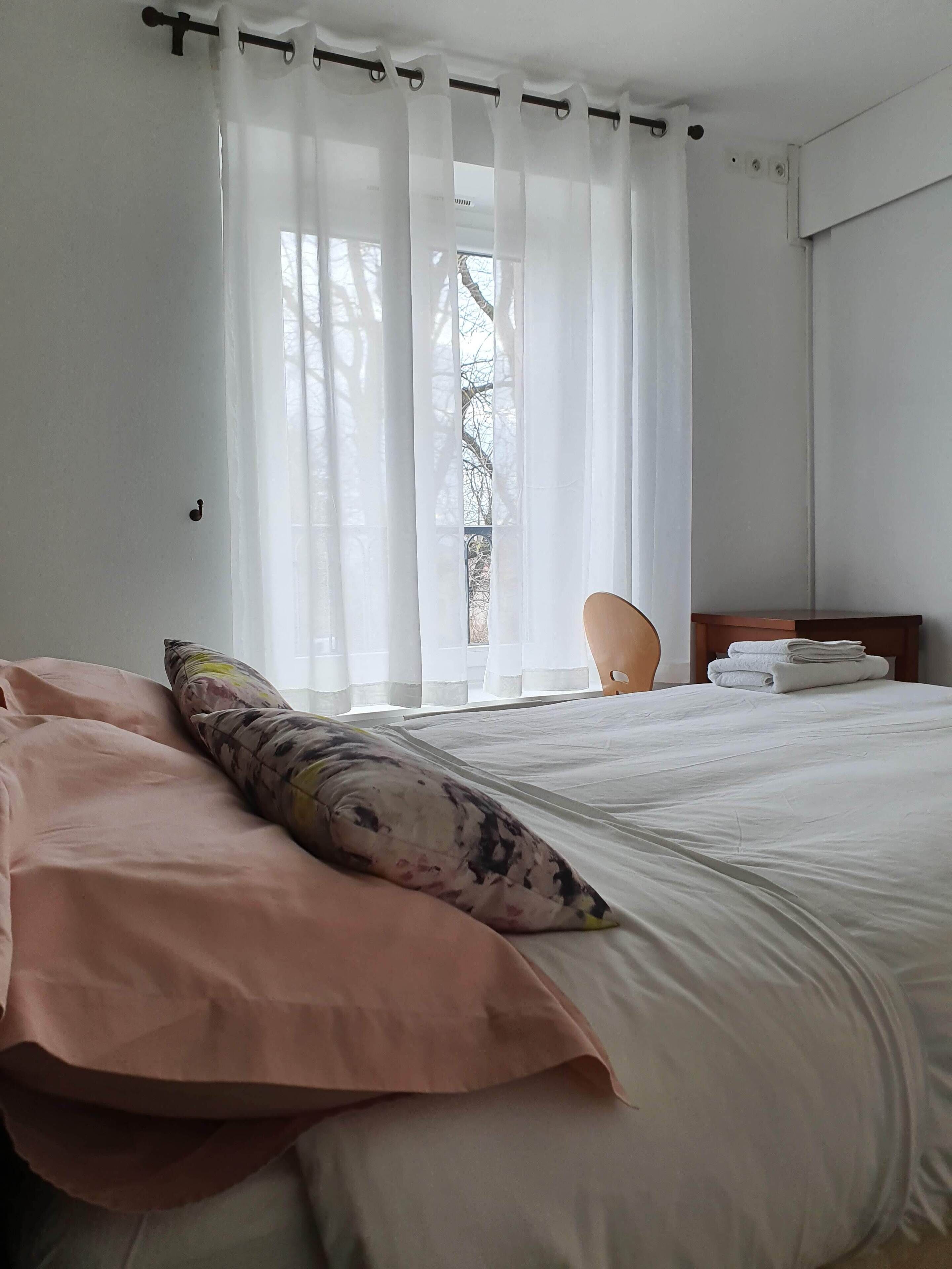 A neatly made bed with a pink and white duvet, a floral pillow, and a wooden nightstand with a folded towel.