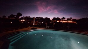 Une vue nocturne d’une piscine, avec un ciel dégagé et des bâtiments situés au loin.
