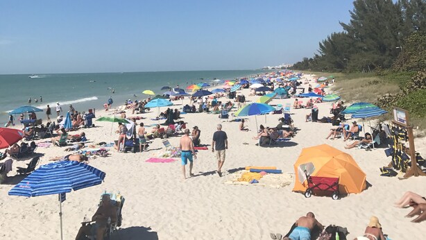 Une plage bondée, avec de nombreux parasols et des gens qui se détendent.