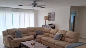 Un salon avec un canapé d’angle beige, une table basse en bois et un ventilateur de plafond.