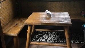 A room with a wooden bench, a small table with a plastic bag, and a window with vertical blinds. - Nipa Hut Tagaytay Get Away for Family & Friends (Amadeo)