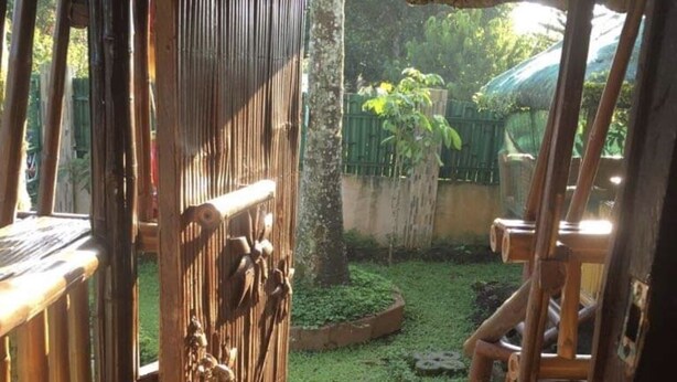 A wooden structure with a thatched roof, leading to a small garden area with a tree and a paved path. - Nipa Hut Tagaytay Get Away for Family & Friends (Amadeo)