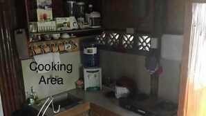 A compact kitchen area with shelves stocked with various kitchen items, a water dispenser, and a small sink. - Nipa Hut Tagaytay Get Away for Family & Friends (Amadeo)