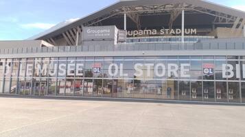 En stadion med en stor glasfasad och skyltar för Groupama Stadium och Olympique Lyonnais-butiken.