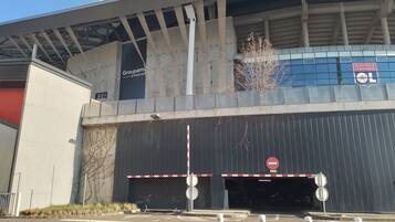 A stadium entrance with a no-entry sign, a Groupama Stadium sign, and a blue building with the Olympic Lyonnais logo.