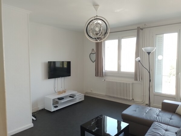 A modern living room with a flat-screen TV, a white entertainment unit, a black marble coffee table, a grey sofa, and a floor lamp. - Apartment near Lyon, Eurexpo and Groupama Stadium  (Vaulx-en-Velin)
