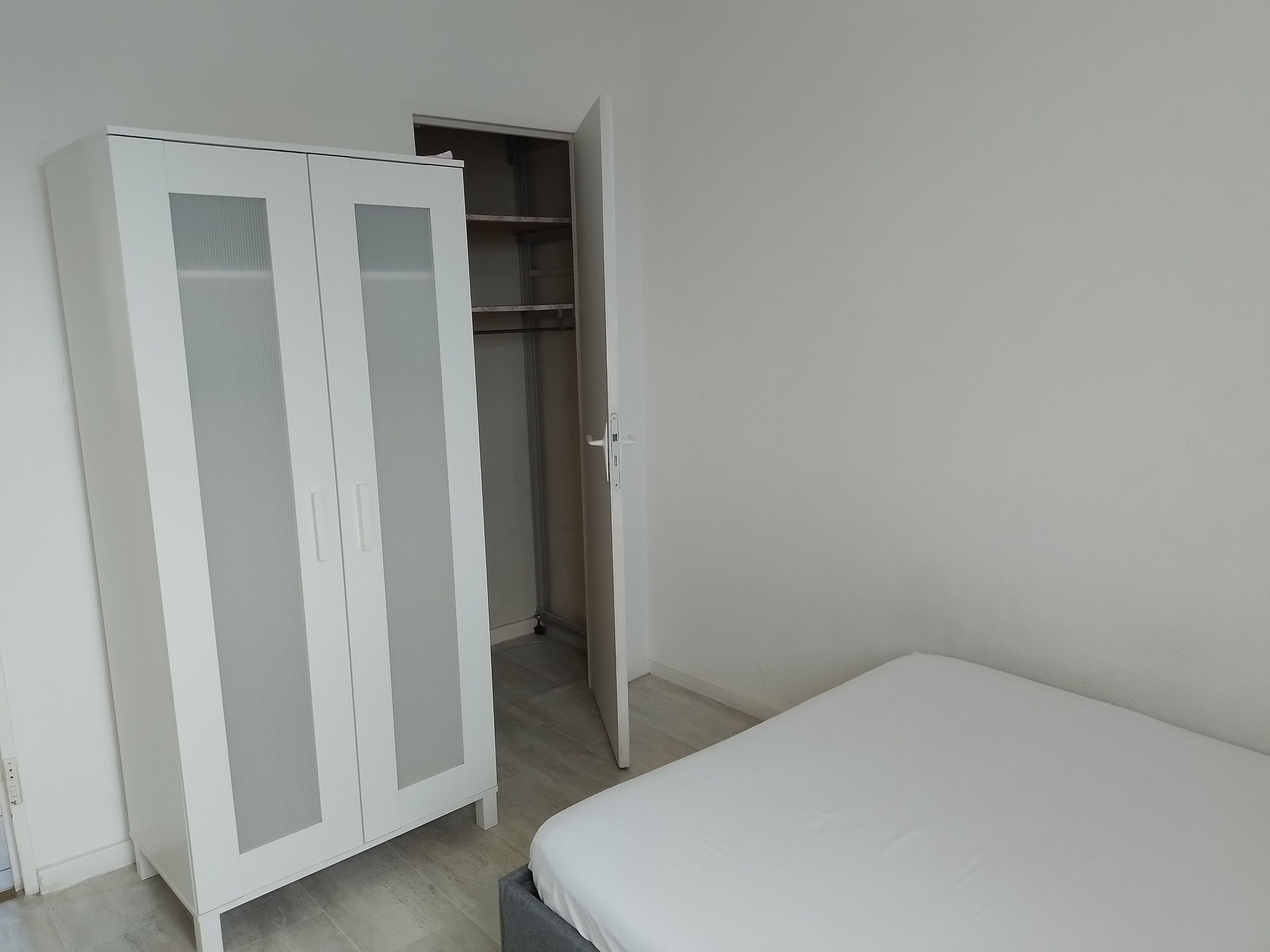 Ein Schlafzimmer mit einem weißen Bett, einem weißen Kleiderschrank mit Glastüren und einem Schrank mit Regalen.