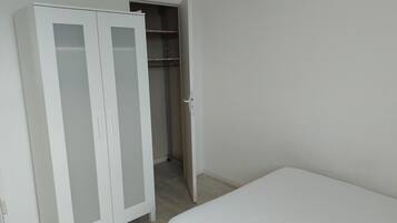 Ein Schlafzimmer mit einem weißen Bett, einem weißen Kleiderschrank mit Glastüren und einem Schrank mit Regalen.
