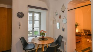 A dining area with a round wooden table, four black chairs, a vase with flowers, a wall clock, and a window with a view of the outside. - !!! COZY APARTMENT 500 FROM THE PALAIS DES PAPES !!! (Avignon)