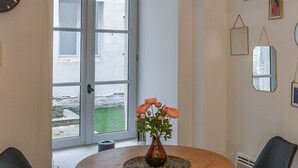 A dining area with a round wooden table, two black chairs, a vase with flowers, and a view through a glass door to the outside. - !!! COZY APARTMENT 500 FROM THE PALAIS DES PAPES !!! (Avignon)