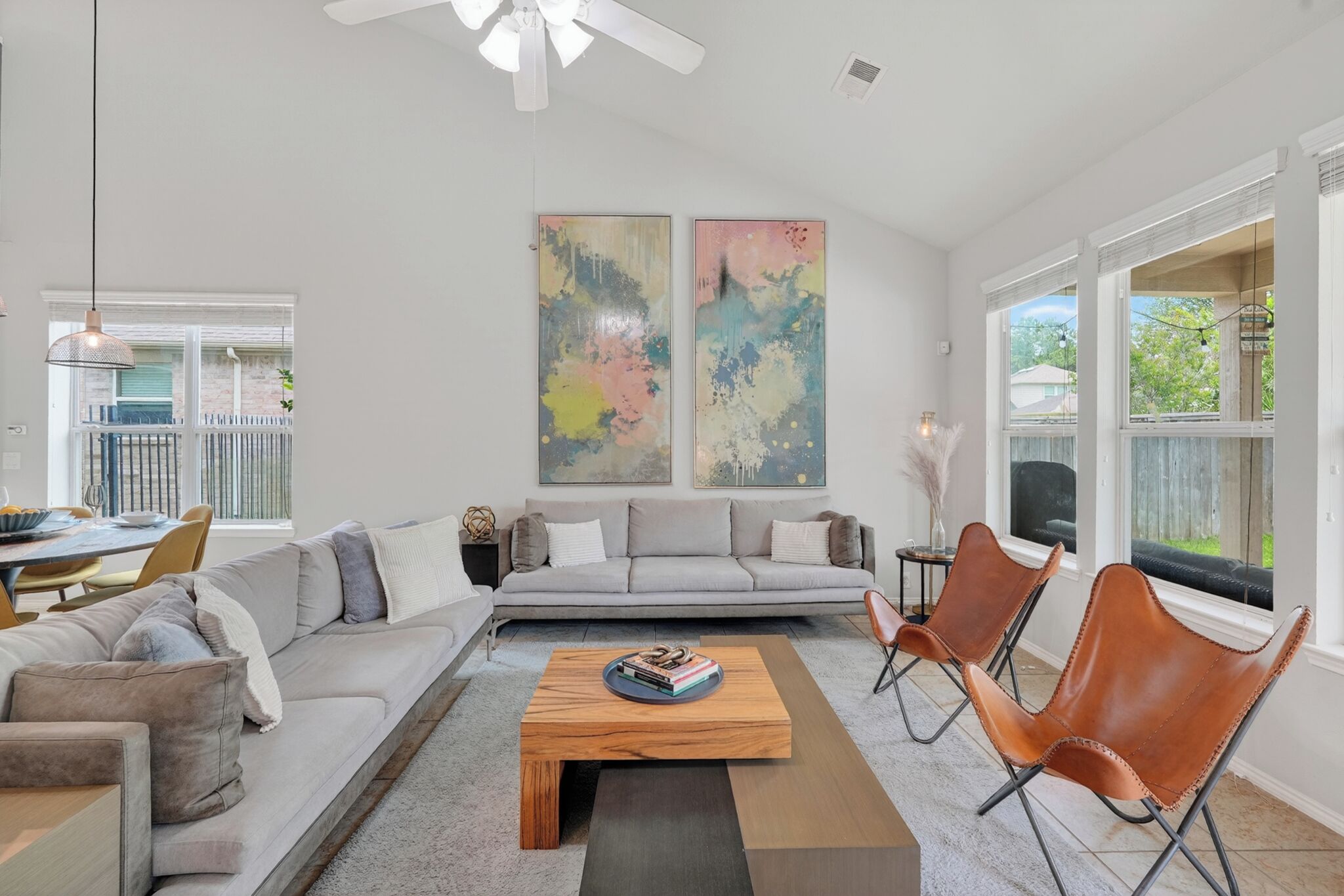 A modern living room with a sofa set, a coffee table, and two chairs. There are abstract paintings on the wall and a balcony visible through the window.