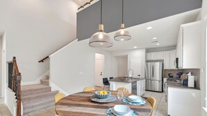 A modern kitchen with stainless steel appliances, a dining area with a wooden table, and a staircase with a wooden railing.