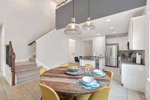 A modern kitchen with stainless steel appliances, a dining area with a wooden table, and a staircase with a wooden railing. - Family friendly w/ beautiful pool, SPA, and BBQ terrace! (Tomball)