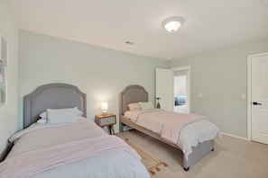 A bedroom with two beds, a nightstand, a lamp, and a door leading to another room. - Family friendly w/ beautiful pool, SPA, and BBQ terrace! (Tomball)