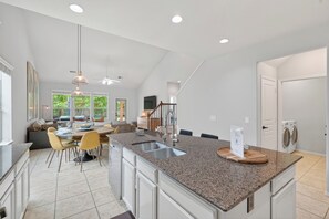 A modern kitchen with granite countertops, a central island with a sink, and a dining area with chairs and a table. - Family friendly w/ beautiful pool, SPA, and BBQ terrace! (Tomball)