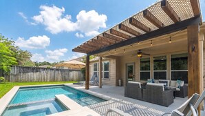 A backyard with a swimming pool, outdoor seating, and a pergola.