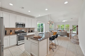 A modern kitchen with white cabinetry, a central island, stainless steel appliances, and a dining area with a view of the outdoors. - Family friendly w/ beautiful pool, SPA, and BBQ terrace! (Tomball)