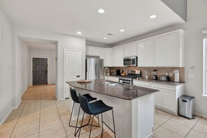 A modern kitchen with white cabinetry, a granite countertop, stainless steel appliances, and a central island with bar stools. - Family friendly w/ beautiful pool, SPA, and BBQ terrace! (Tomball)