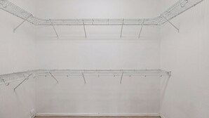 A closet with two metal wire shelves, a beige carpet, and white walls.
