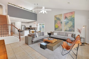 A modern living room with a sofa, coffee table, and chairs, a staircase, and a kitchen in the background. - Family friendly w/ beautiful pool, SPA, and BBQ terrace! (Tomball)