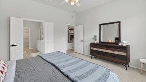 Een slaapkamer met een bed, een dressoir, een spiegel en een plafondventilator.