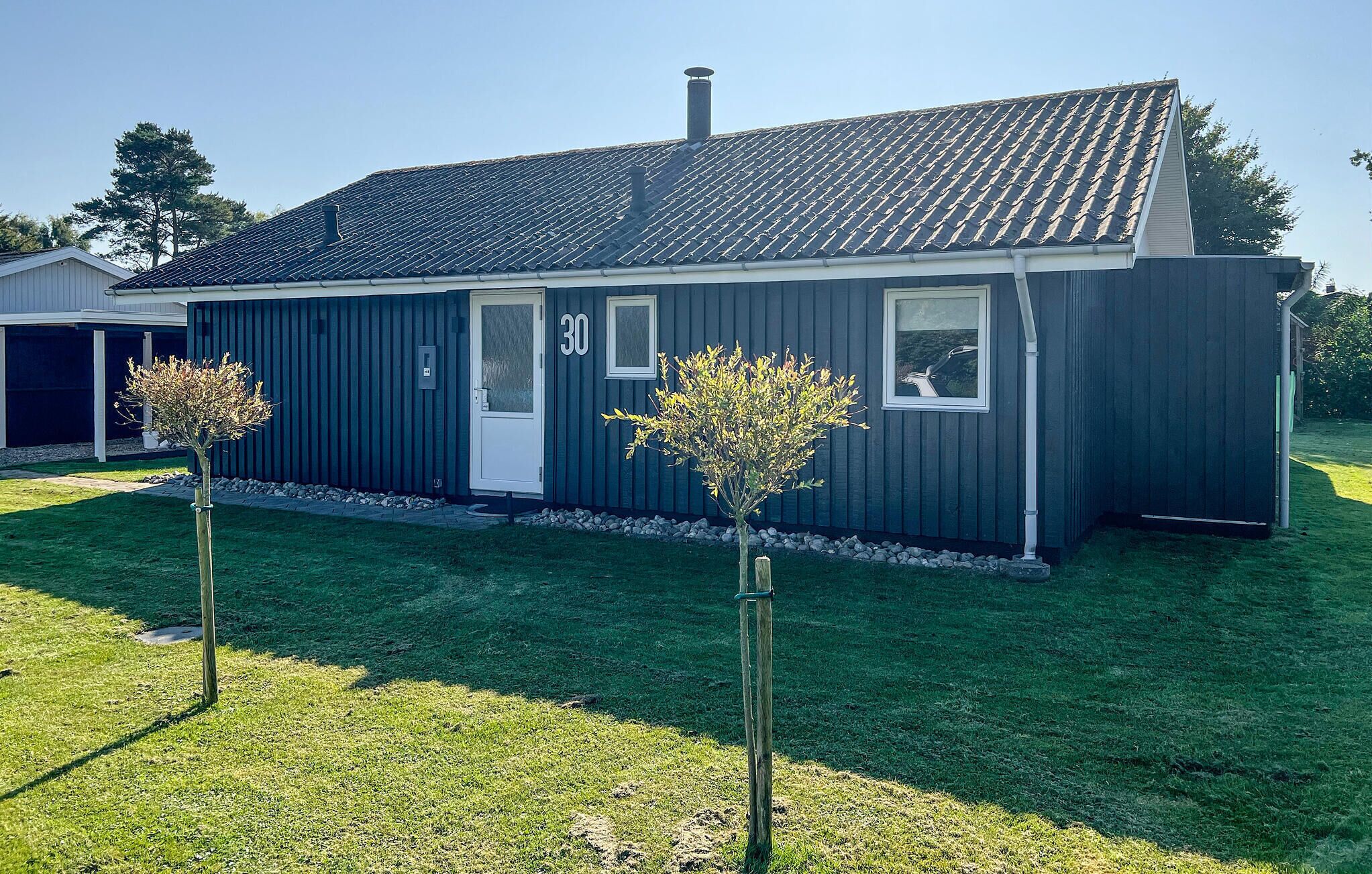 A single-story house with a dark blue exterior, a white door, and a small window. There are two trees in the front yard.