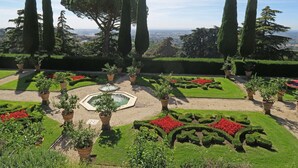 Un jardin à la française, avec des haies aux formes géométriques, une fontaine centrale et de grands cyprès.