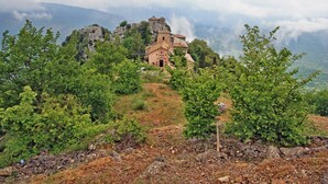 Une église rustique, perchée sur une colline, entourée d’une végétation luxuriante et d’un paysage rocheux.