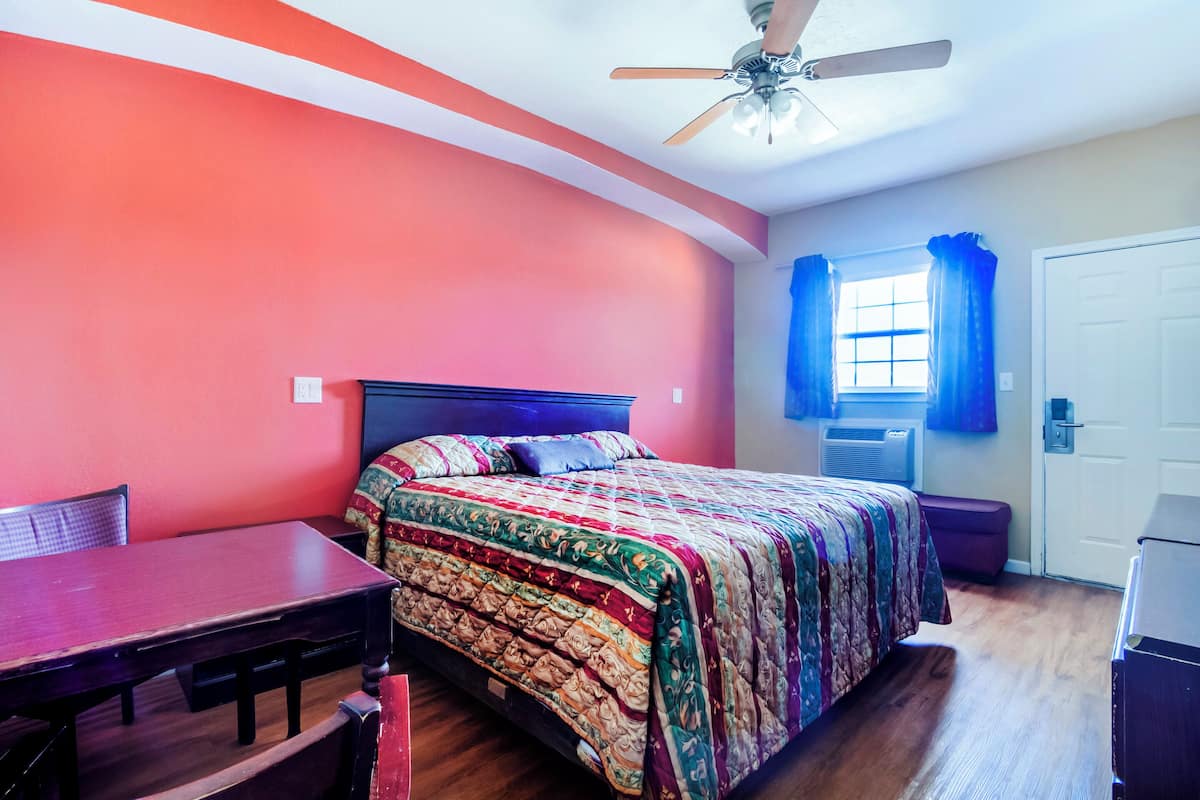 A room with a bed, a table, and a ceiling fan.
