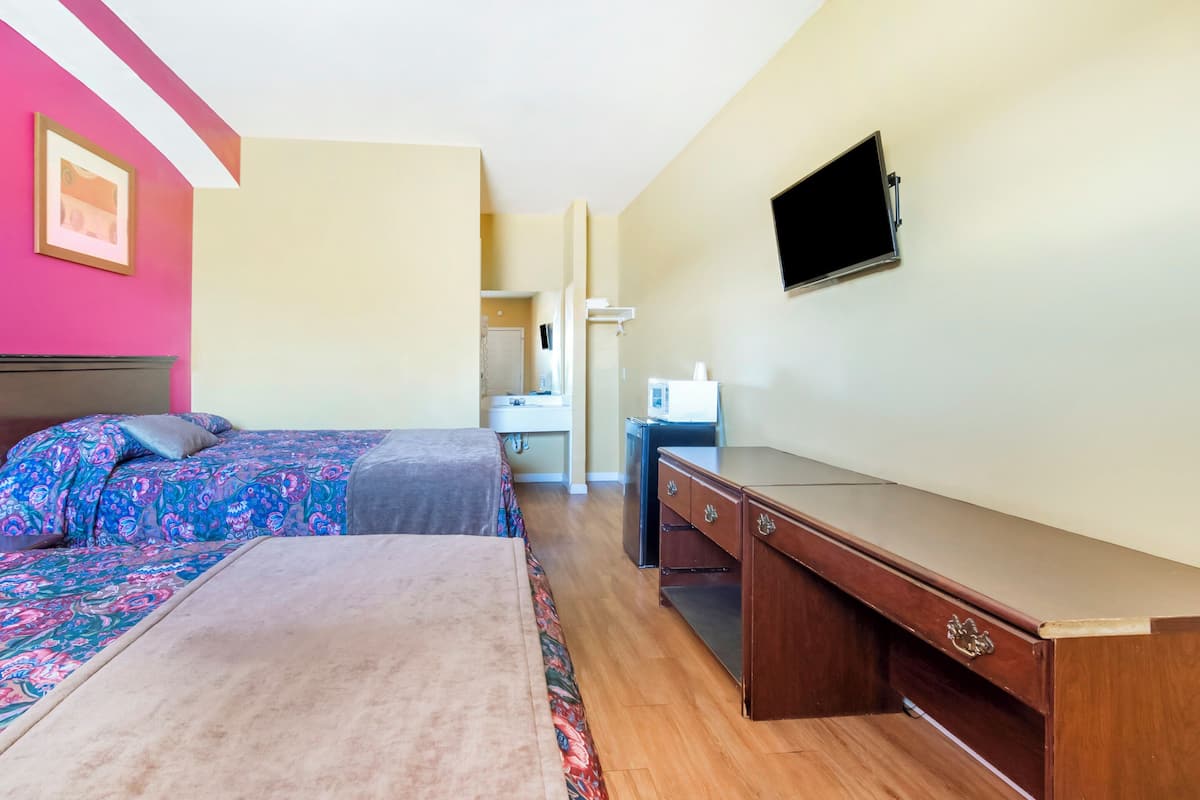 A hotel room with two beds, a desk, a television, and a bathroom visible in the background.