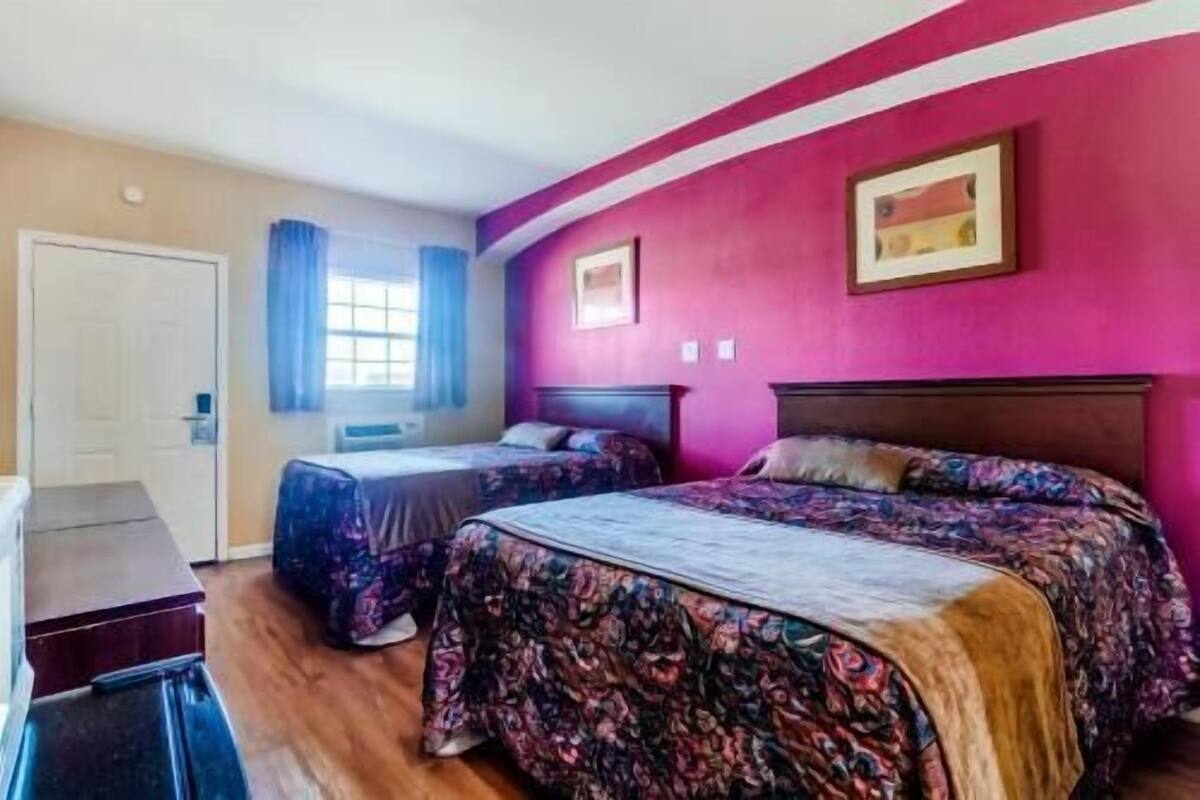 Una habitación con dos camas, una ventana con cortinas azules y una puerta.
