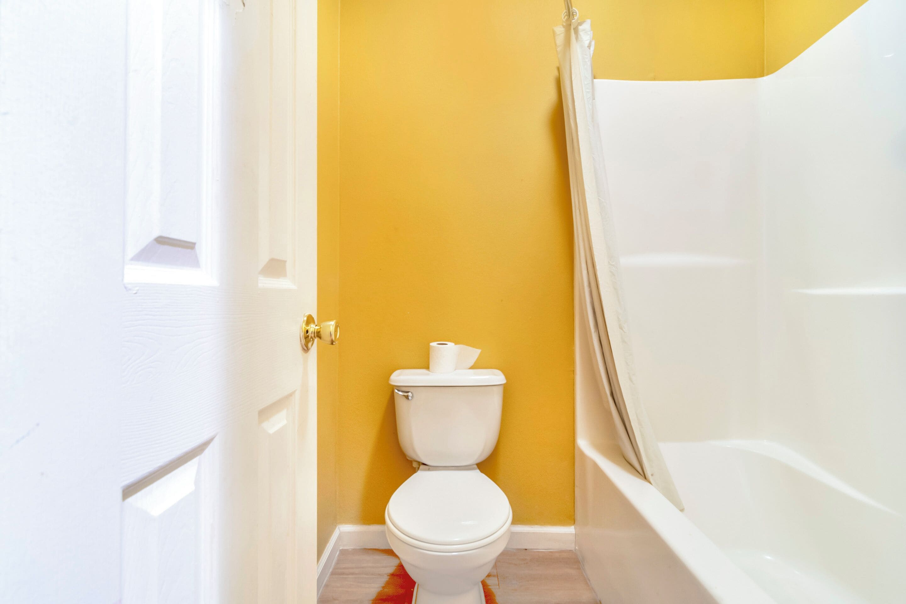 Une salle de bain avec des toilettes blanches, une baignoire et un mur jaune.
