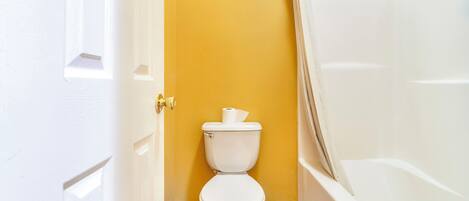 Une salle de bain avec des toilettes blanches, une baignoire et un mur jaune.
