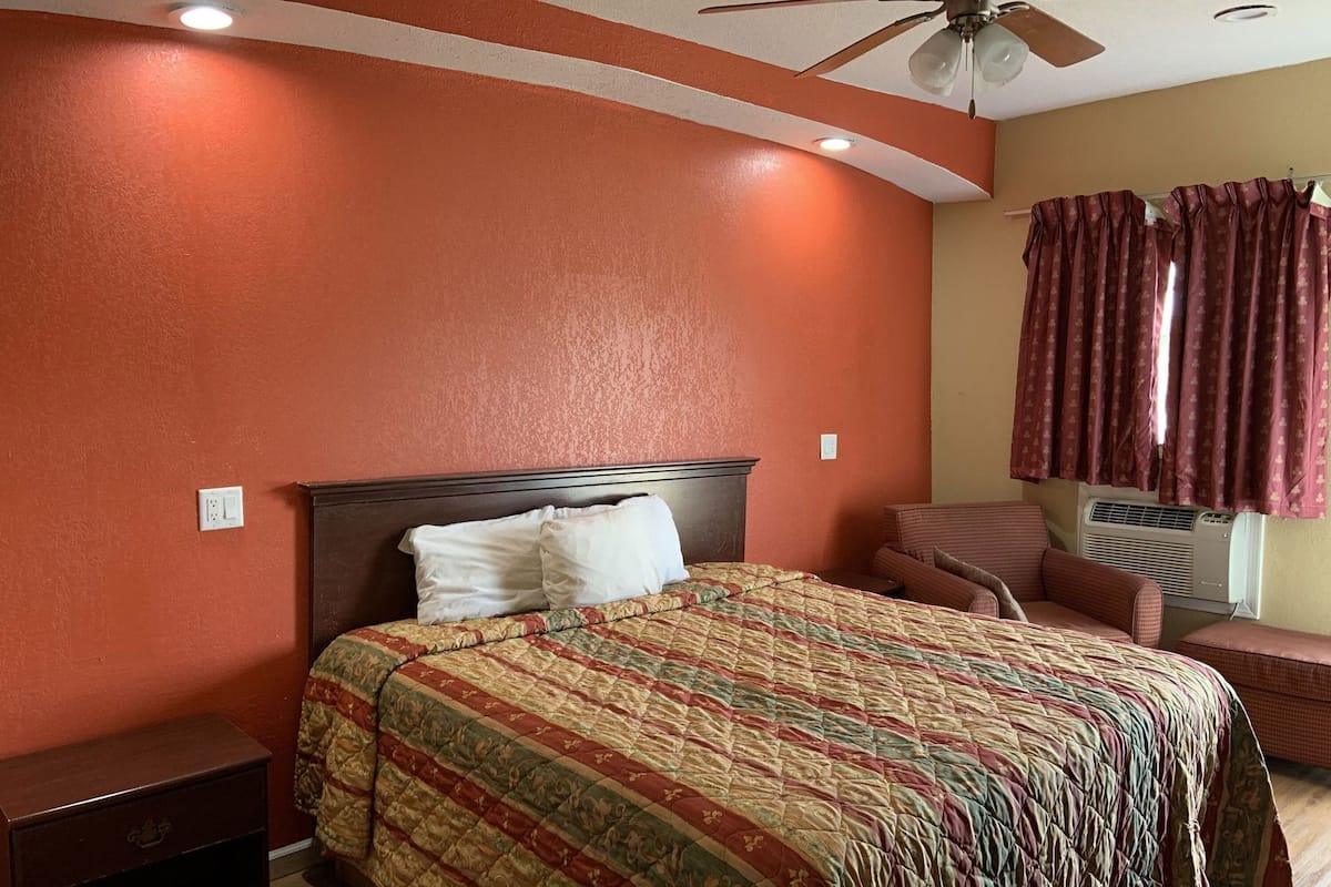 A bedroom with a bed, a nightstand, a ceiling fan, and a window with curtains.