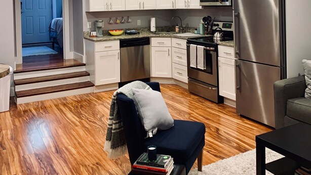 A modern kitchen with white cabinets, stainless steel appliances, and a wooden floor.